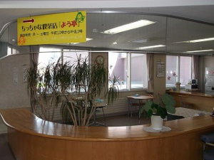 介護施設のロビー・受付エリア。木製カウンター、観葉植物、黄色の看板が見える